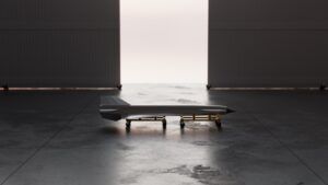 Rendering of the slender, dart-shaped Ramjet-X hypersonic test vehicle on a wheeled cradle in a darkened hangar, with light coming through the open doorway