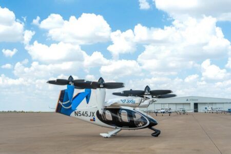 Joby flies Texas eVTOL routes to shape commercial airspace rules A Joby electric air taxi with a Texas flag on its tail parked on the ramp at Perot Field Fort Worth Alliance Airport, with a hangar behind