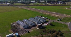 Aerial view of the drone testing facility at Westcott Venture Park, with hangars, a control building, parking and a test area beside a runway in open countryside