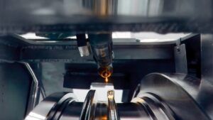 A close-up of a laser deposition head inside a machine, with a glowing molten pool as metal is built up onto a component