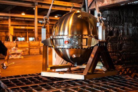 NASA’s Venus descent probe passes furnace heat tests Polished stainless steel spherical probe suspended by lifting straps above a metal furnace tray in an industrial workshop
